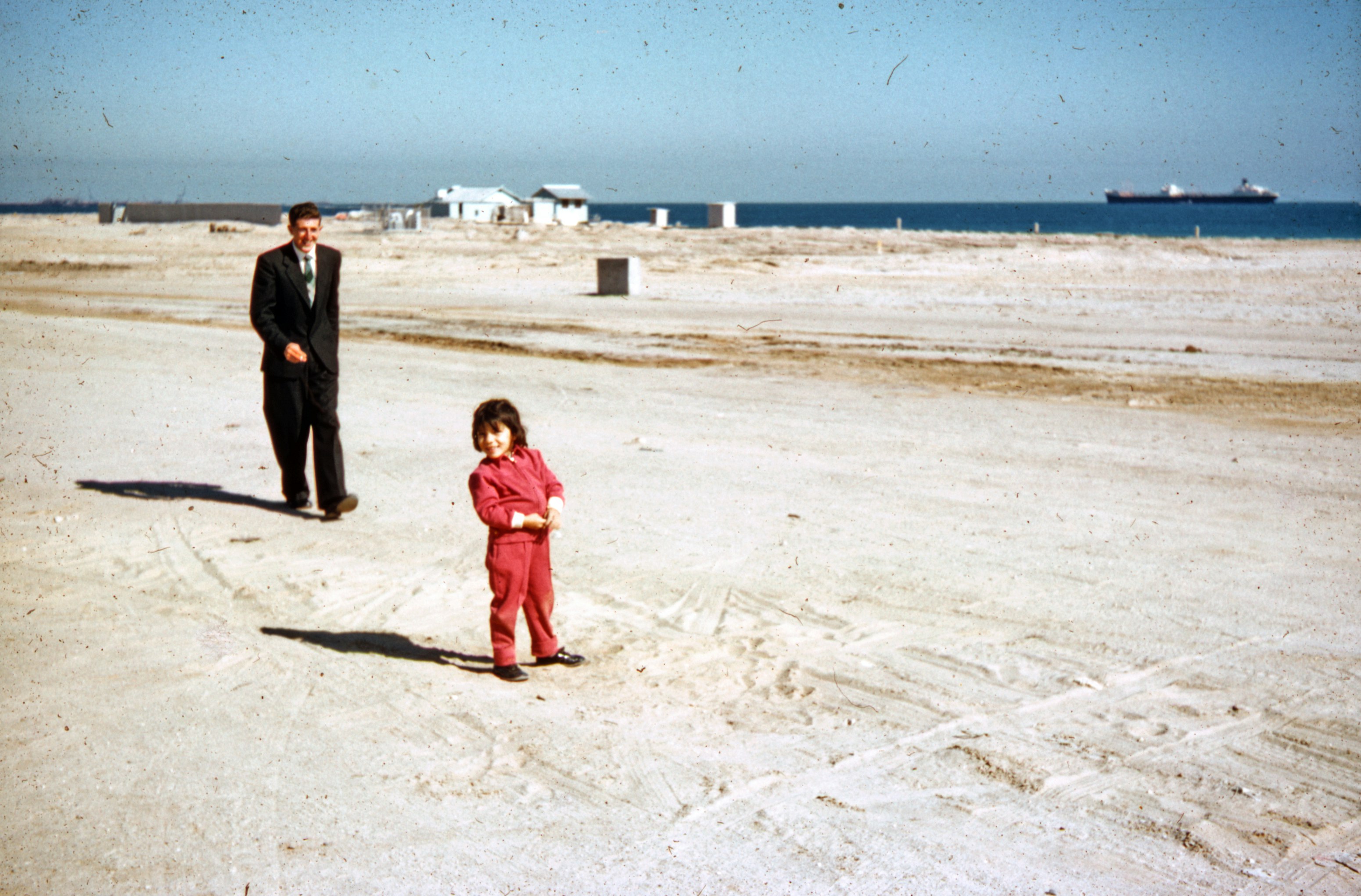 woman in red coat standing beside man in black suit on beach during daytime